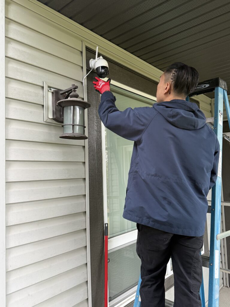 Technician installing an outdoor security camera beside a home entrance