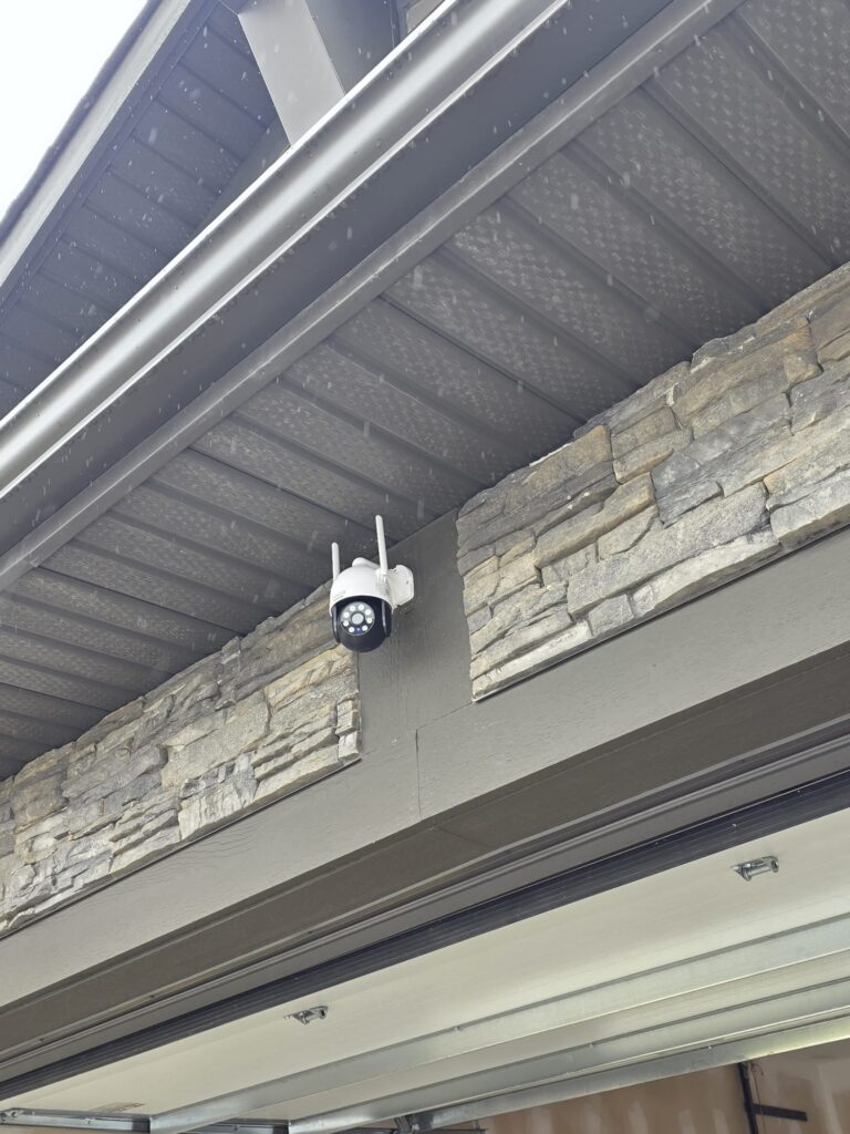 Outdoor security camera installed above a Calgary home garage door beside stone cladding